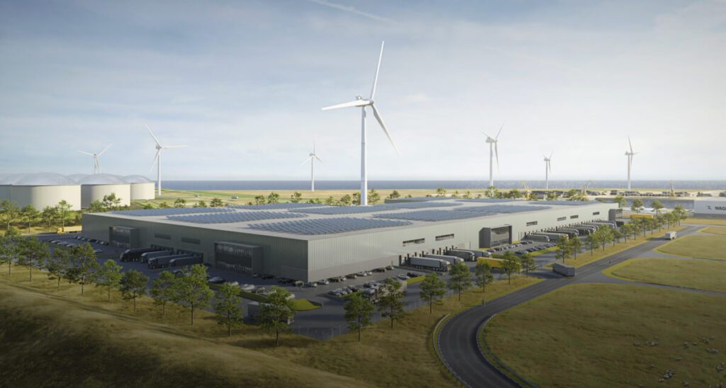 large industrial facility next to a body of water with wind turbines