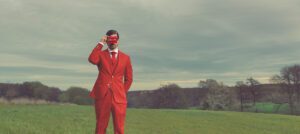 Picture with a men in a red suit making a picture with a red polaroid camera on a field
